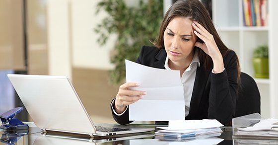 Stressed Out Woman Reading Paperwork in Front of her work laptop